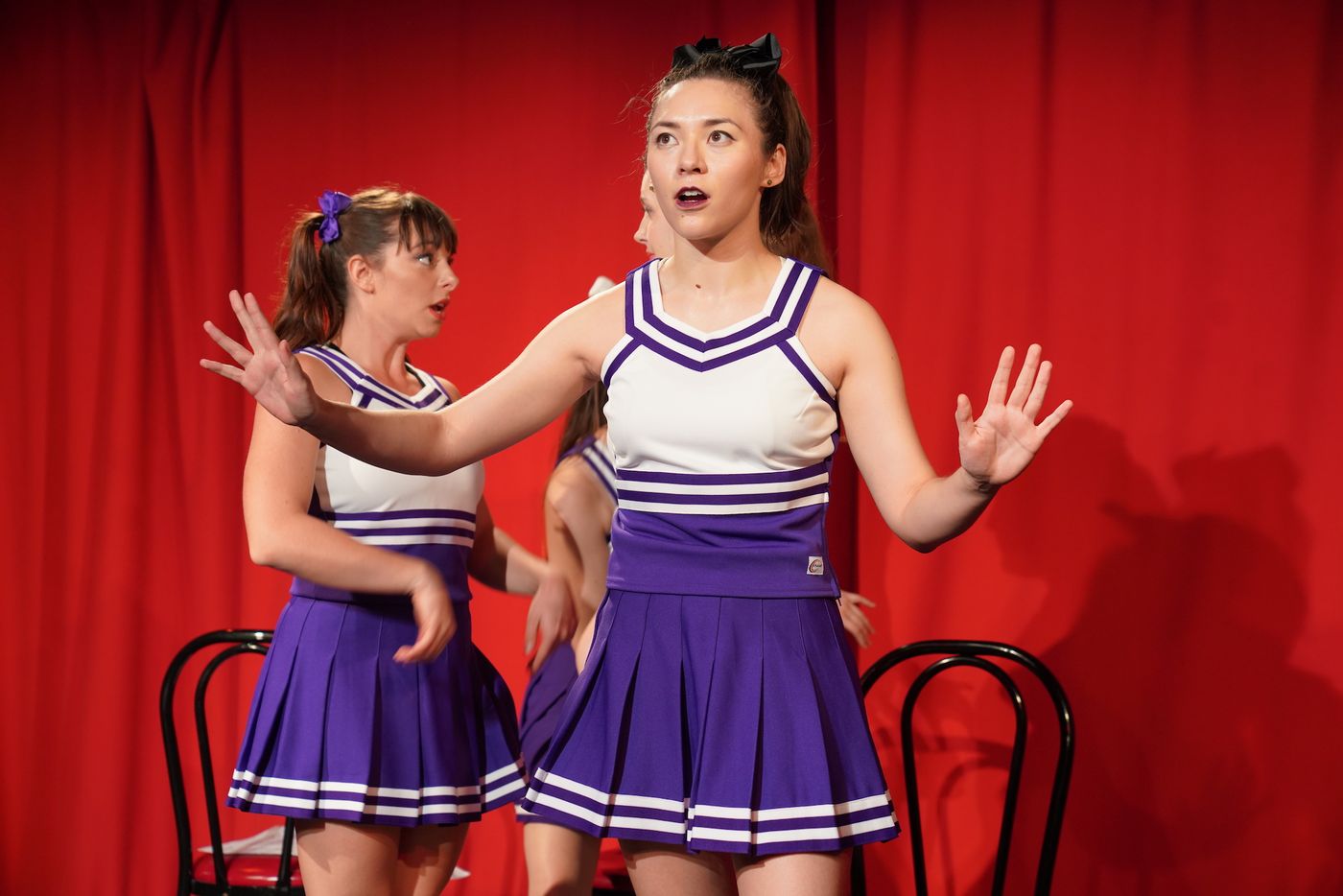 Two cheerleaders on stage, one with her hands raised in surprise.