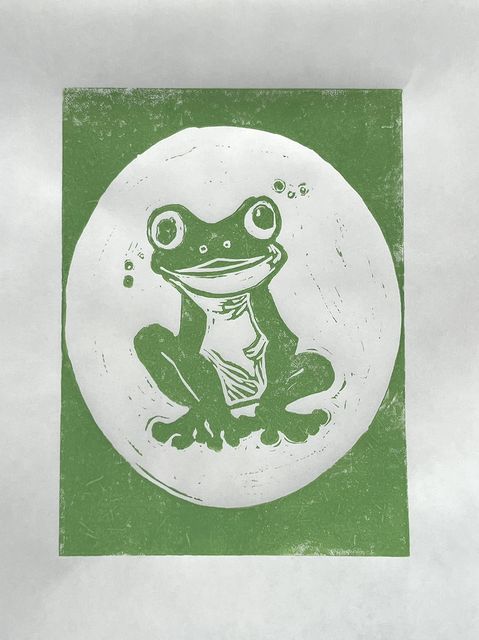 Green linocut print of a smiling frog sitting inside a white oval.