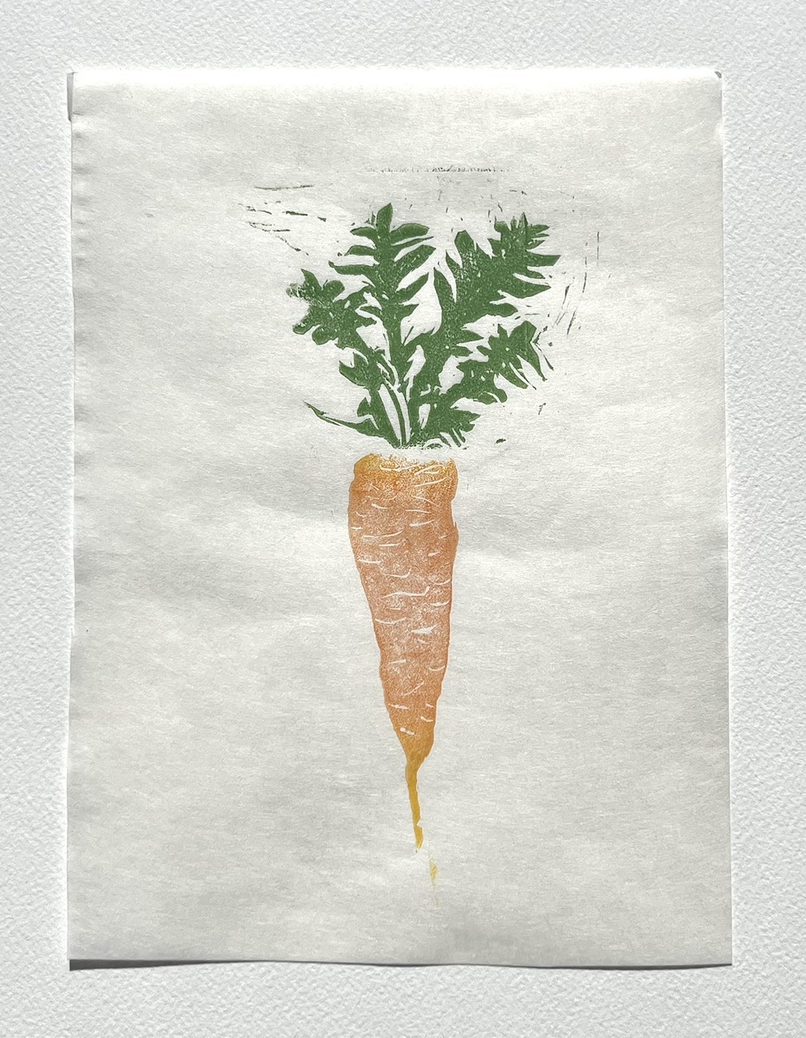 Linocut print of a carrot with a leafy green top, printed in orange and green ink on white Japanese paper.