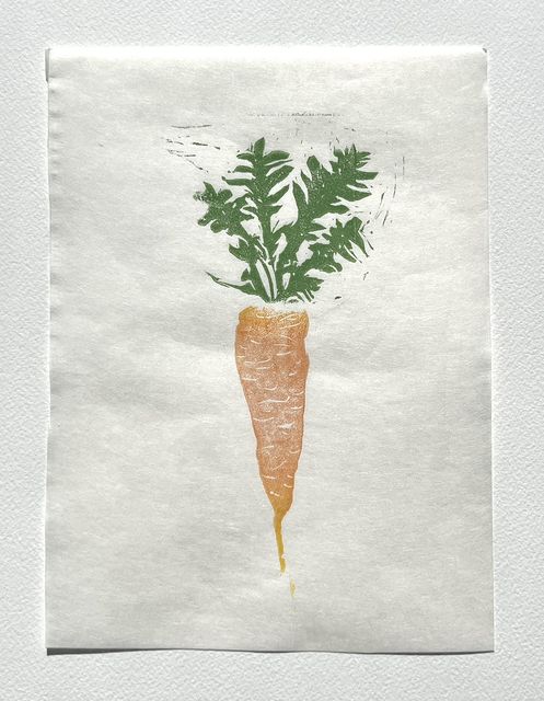 Linocut print of a carrot with a leafy green top, printed in orange and green ink on white Japanese paper.